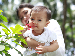 Woman holding a baby up to smell a flower