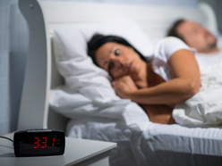 Woman in bed looking at the clock which says 3:31am.