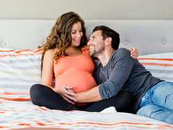 an overdue pregnant woman with her partner on a bed cuddling in an attempt to bring on labour