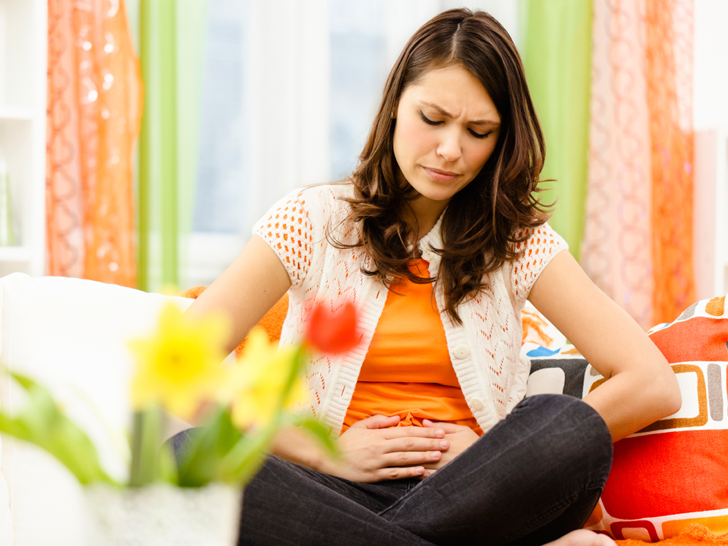 pregnant woman with abdominal pain sitting on a couch with her hands on her belly and looking pained
