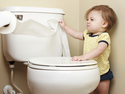 angry toddler standing next to a toilet and pulling toilet paper