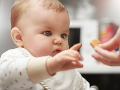 baby in a highchair reaches for food in an adult's hand