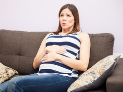 pregnant woman sitting on her couch with her hands over her belly and looking pained