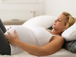 Pregnant woman in bed looking fed up.