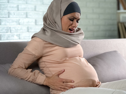 Pregnant woman sitting on the sofa and grimacing in pain