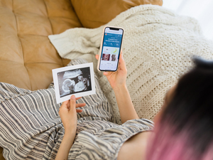 A pregnant woman sitting on the couch looking at a sonogram and the BabyCenter app.