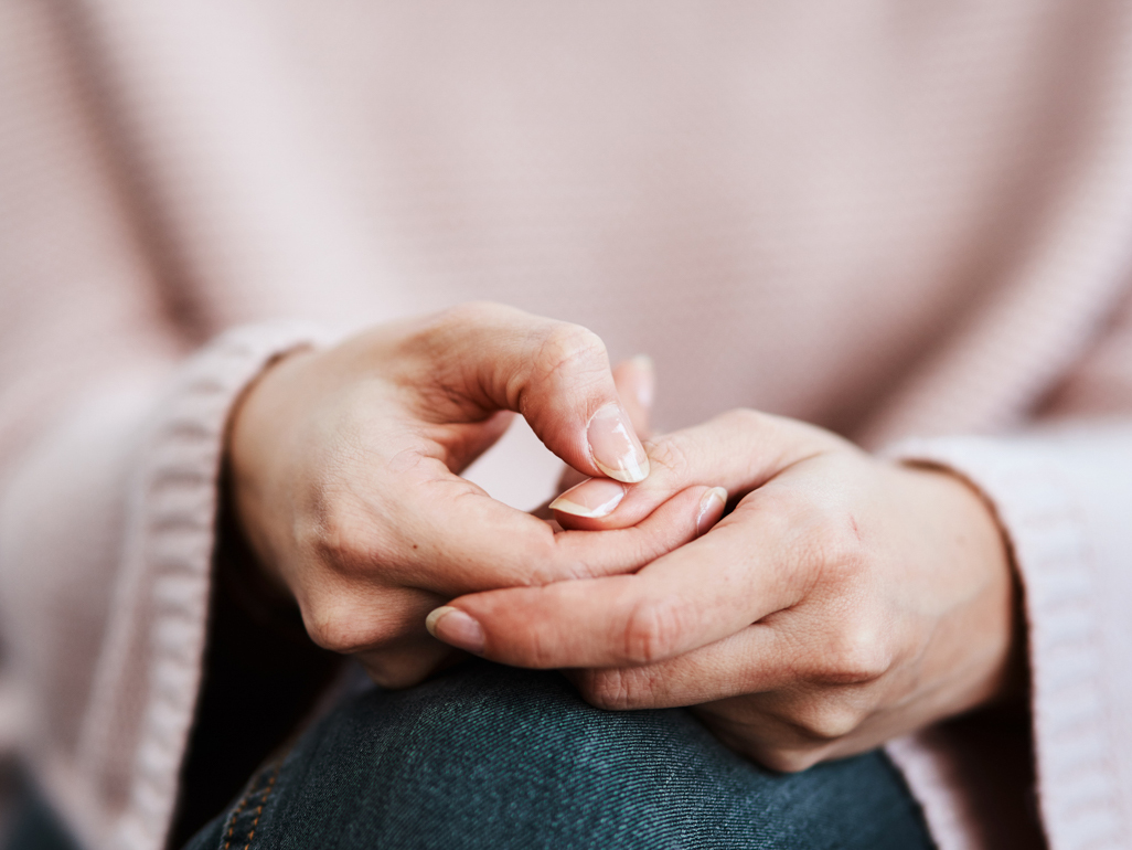 A close up of a woman with anxiety picking at her fingernails.