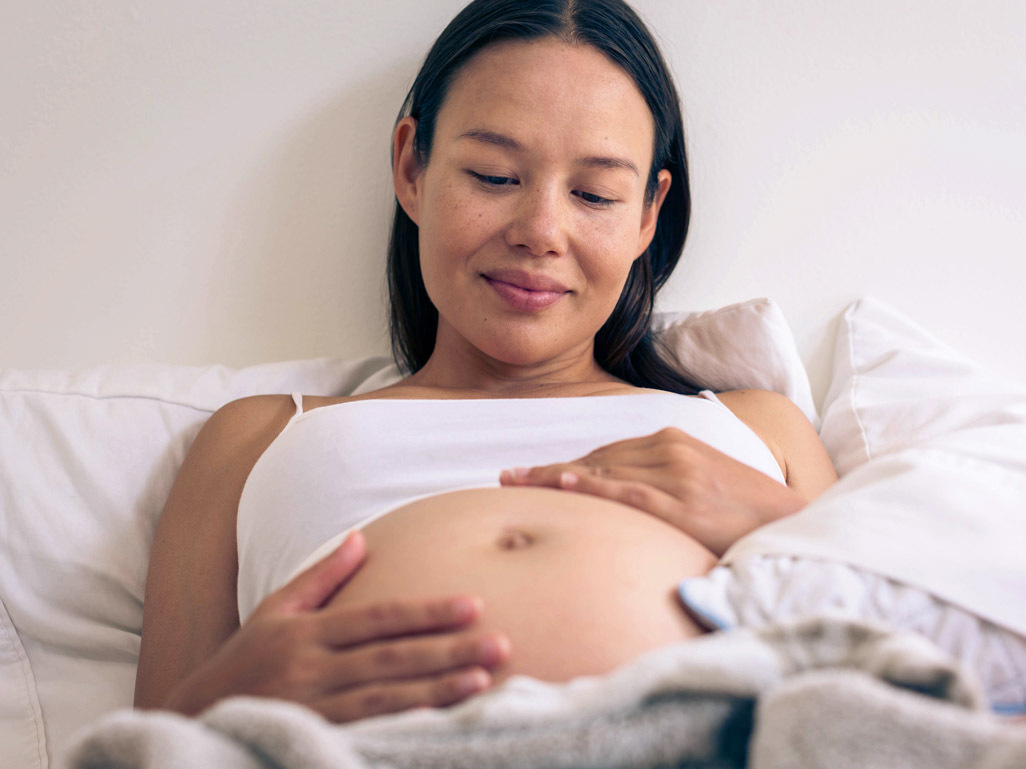 Pregnant woman smiling with hands on bump