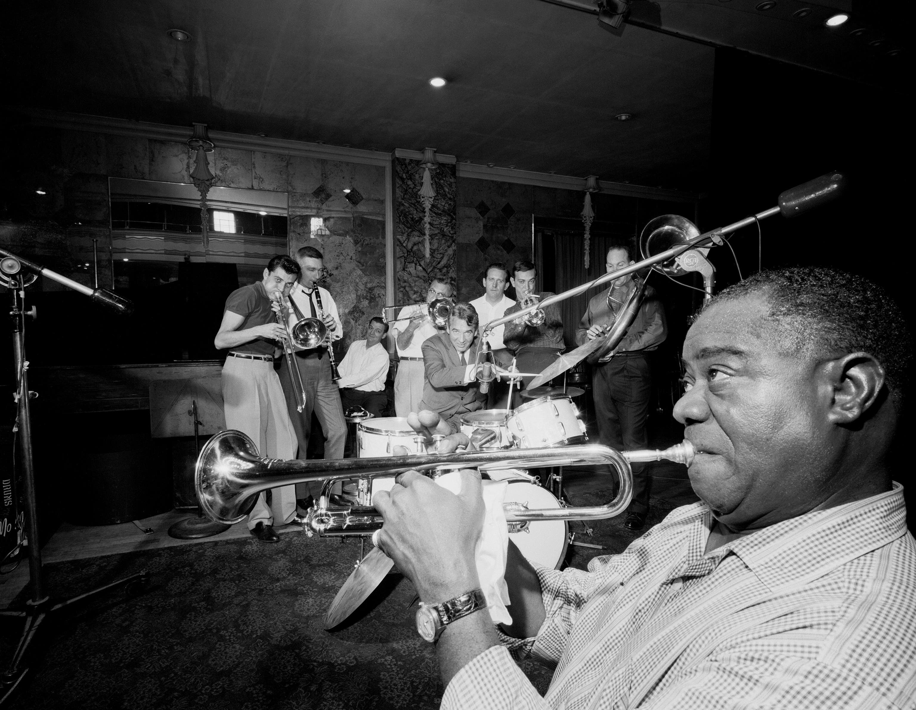 UNITED STATES - CIRCA 1920: Louis Armstrong (r.), who reshaped jazz in the 1920s and was still picking up new fans into the 1960s with his renditions of pop songs such as &quot;Hello, Dolly&quot; and &quot;Mack the Knife,&quot; plays the trumpet at a rehearsal for a recording date in early 1960 with the Dukes of Dixieland. Trumpeter Frank Assunto (background, 2nd from right) and his brother Fred (far l.) put that band together in the late 1940s to help revive the earliest form of traditional jazz, born in their native New Orleans. That&#039;s another jazz legend, Gene Krupa, sitting at the drums; the Assuntos&#039; father, Pap Jac, is the trombonist behind Krupa. The others in the band are (left to right) Jerry Fuller, on clarinet; Stanley Mendelson, at the piano; Owen Mahoney, the bands&#039; regular drummer; and Richard Matteson, handling bass. (Photo by NY Daily News Archive via Getty Images)