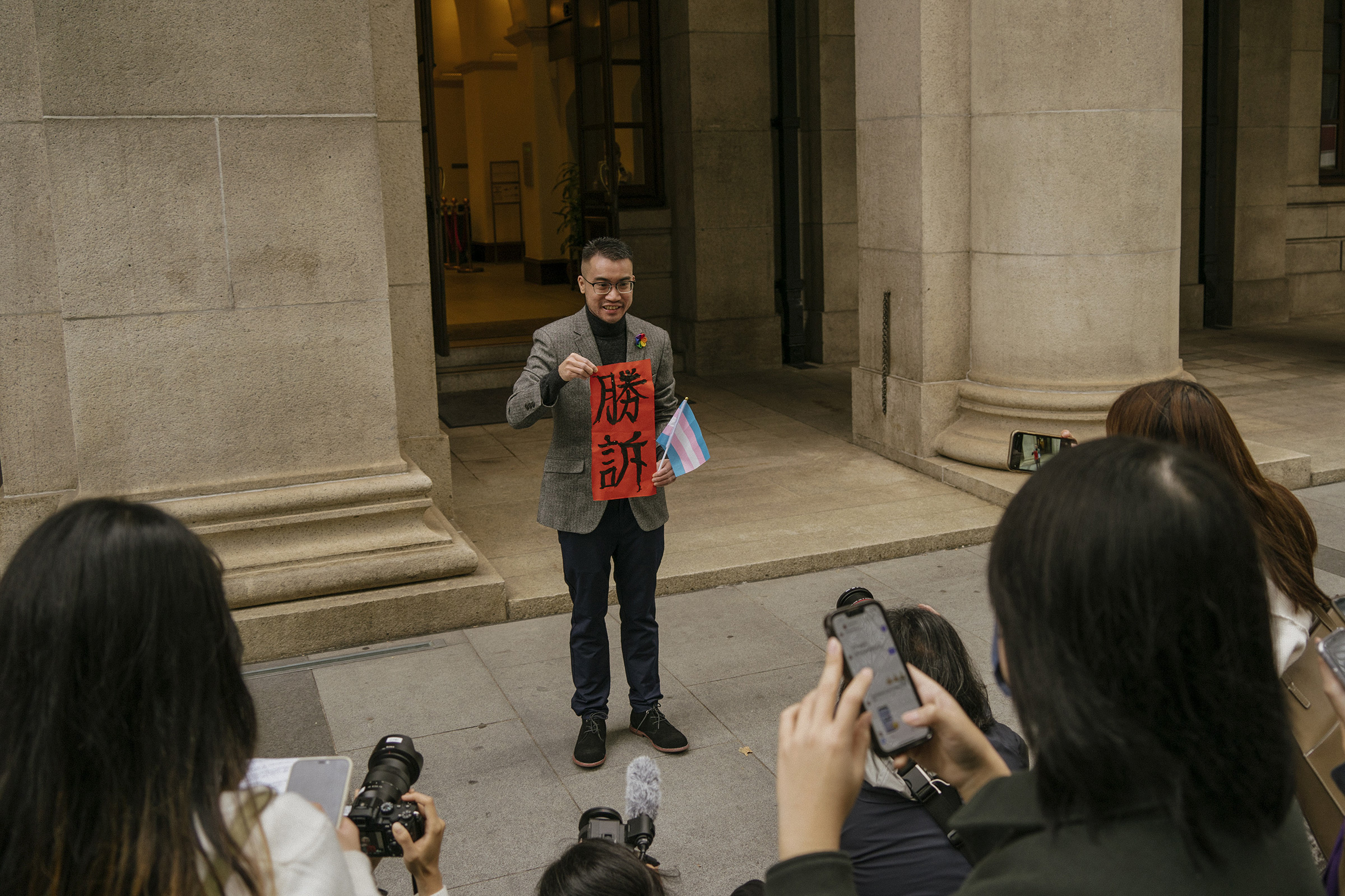 Henry Edward Tse holds a sign saying 'Legal Victory' and a transgender flag while speaking to reporters outside of the Court of Final Appeal in Hong Kong, Feb. 6, 2023.