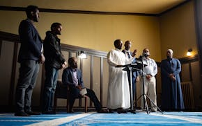 Osman Ahmed sits down due to his injuries while Alhikma Islamic Center Imam Abdirazak Kaynan speaks Friday in Minneapolis at a news conference about a