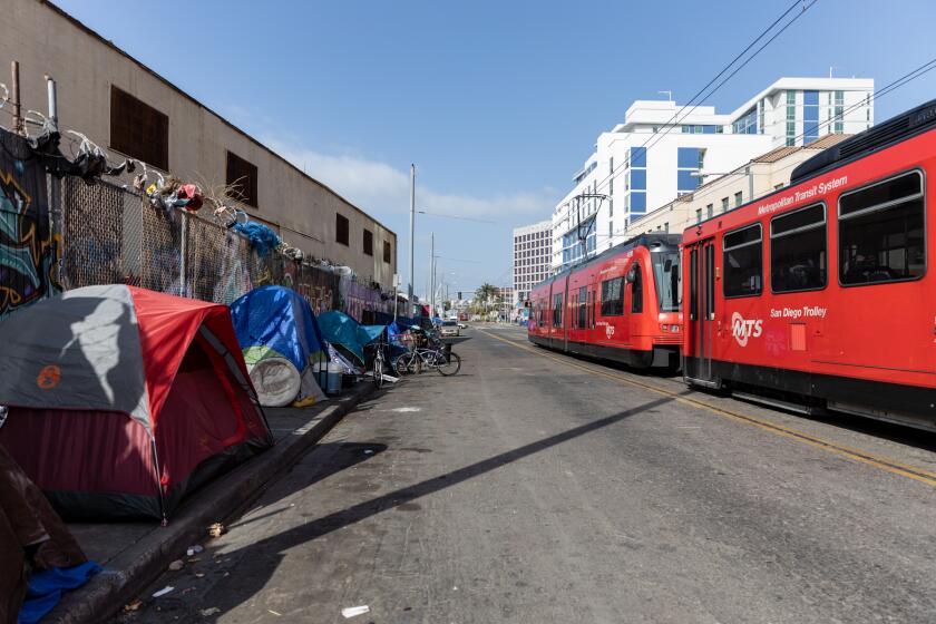 A trolley passes by a homeless encampment on Commercial Street in downtown San Diego on Thursday, March 10, 2022. In this area, a pilot program called the Triangle Project, pays people experiencing homelessness $2 for each bag of litter they collect. The program, started by San Diegan Brian Trotier and funded by non-profit Lucky Duck Foundation, will run every Monday and Thursday for the next four months.