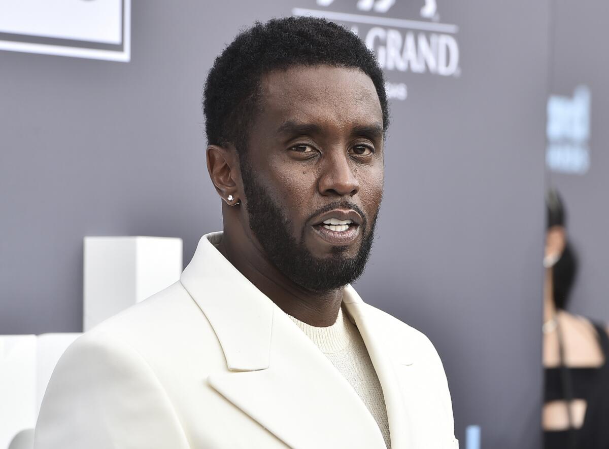 Sean Combs poses at an event in a cream suit.