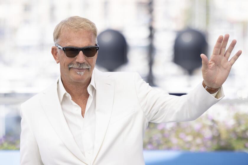 Kevin Costner waves in white suit and sunglasses on Cannes red carpet