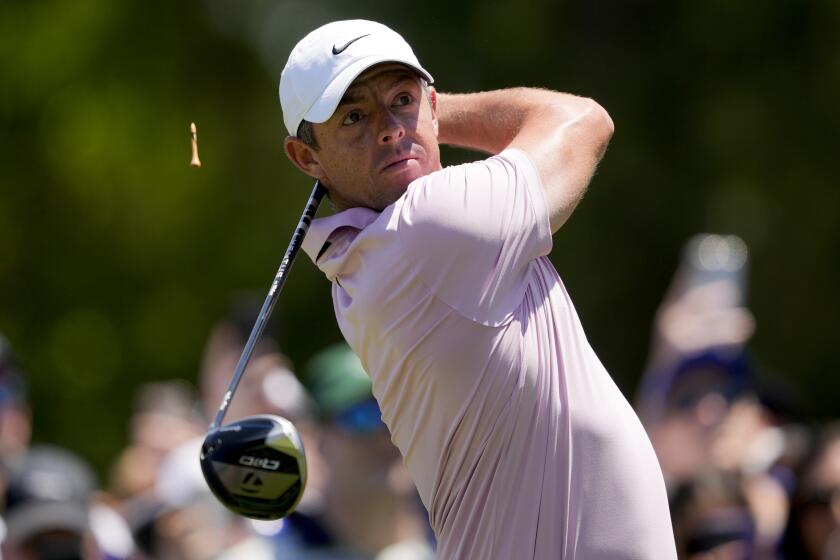 Rory McIlroy, in a white hat and pink polo shirt, swings his golf club