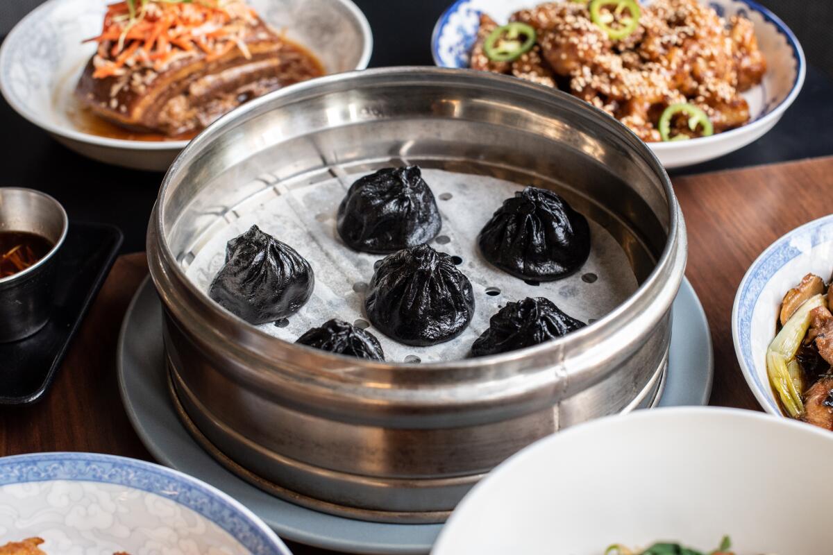A round steamer dish holds black dumplings, surrounded by other dishes on a table