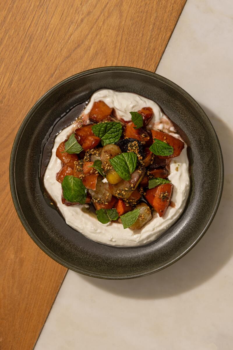 A round dish of roasted carrots atop a creamy yogurt-y base, resting on a two-toned table.