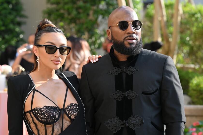 Jeannie Mai in sunglasses and a sheer, black gown holding Jeezy who is wearing sunglasses and a black suit