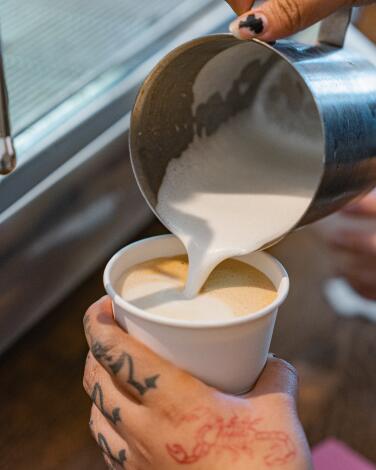 Pouring frothed milk into a paper cup of coffee.