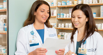 Two female pharmacists reviewing document in front of shelves of medications