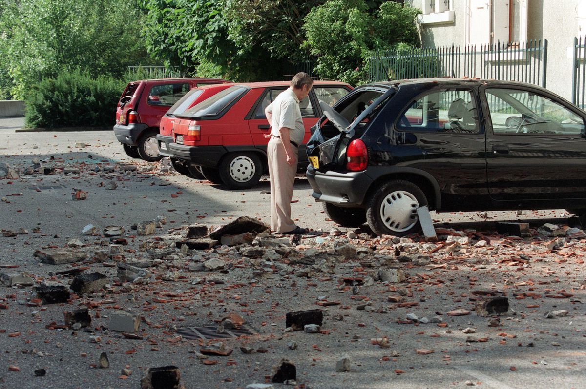 Un homme constate les dégâts occasionnés sur son véhicule par la chute de tuiles, suite à un séisme d'une magnétude de 5,2 qui s'est produit au cours de la nuit, le 15 juillet 1996 à Annecy. (Photo by GERARD MALIE / AFP)
