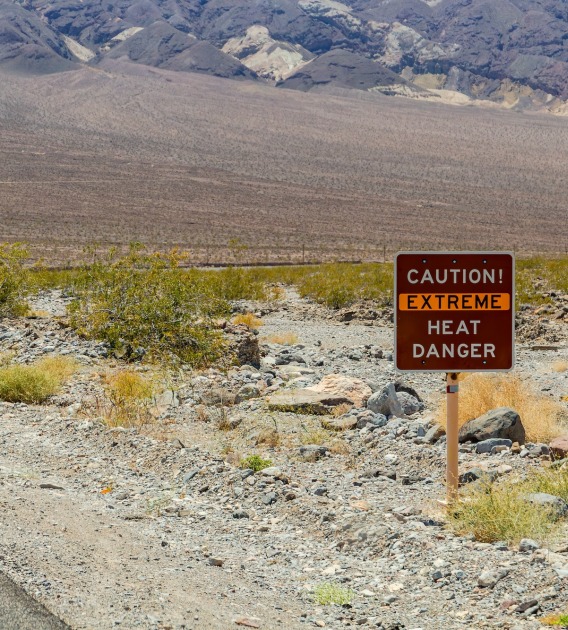 a sign that says "caution extreme heat danger" next to a road in a desert
