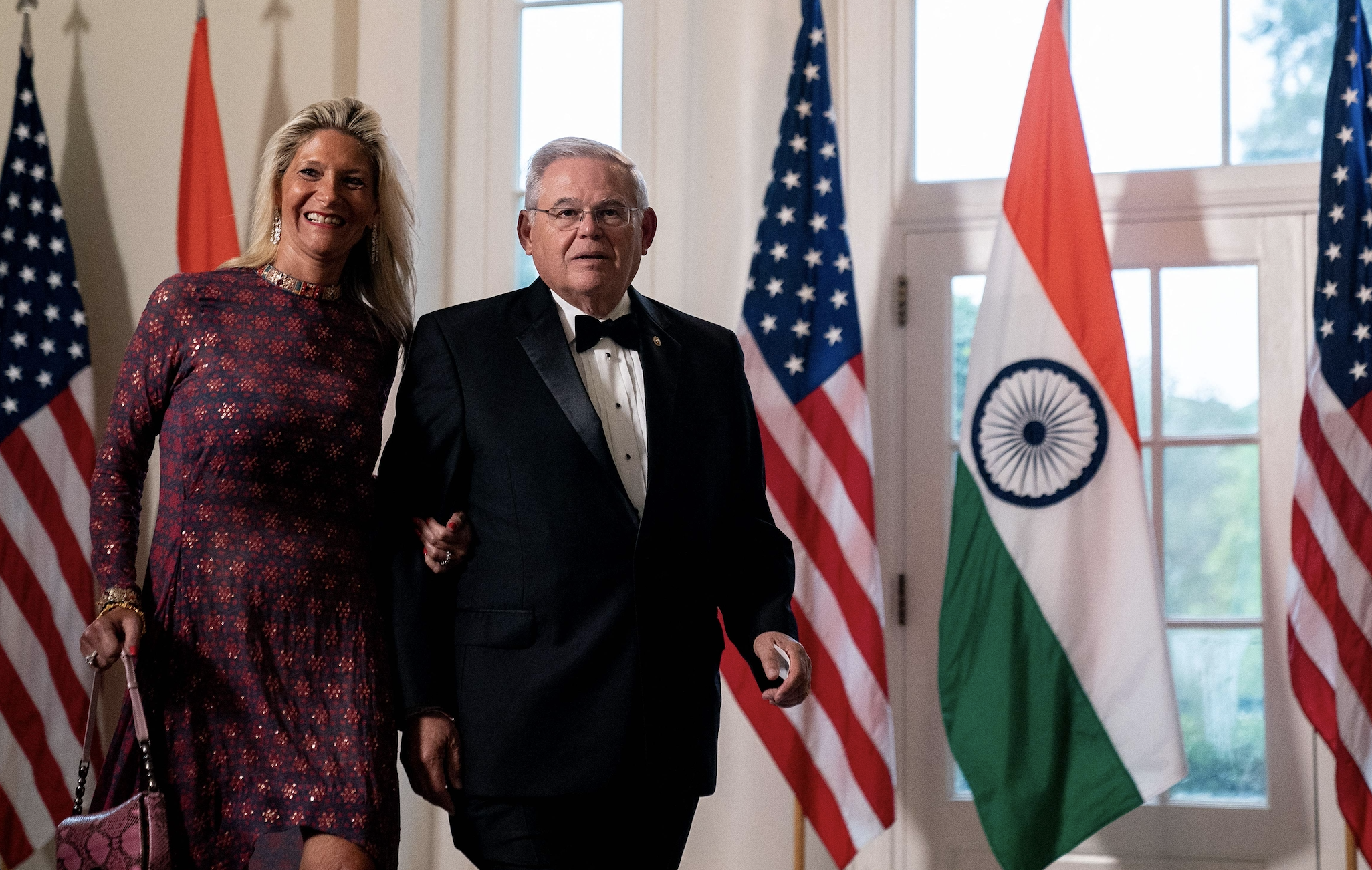 Bob Menendez and his wife stand inside the White House in front of a row of US and India flags.