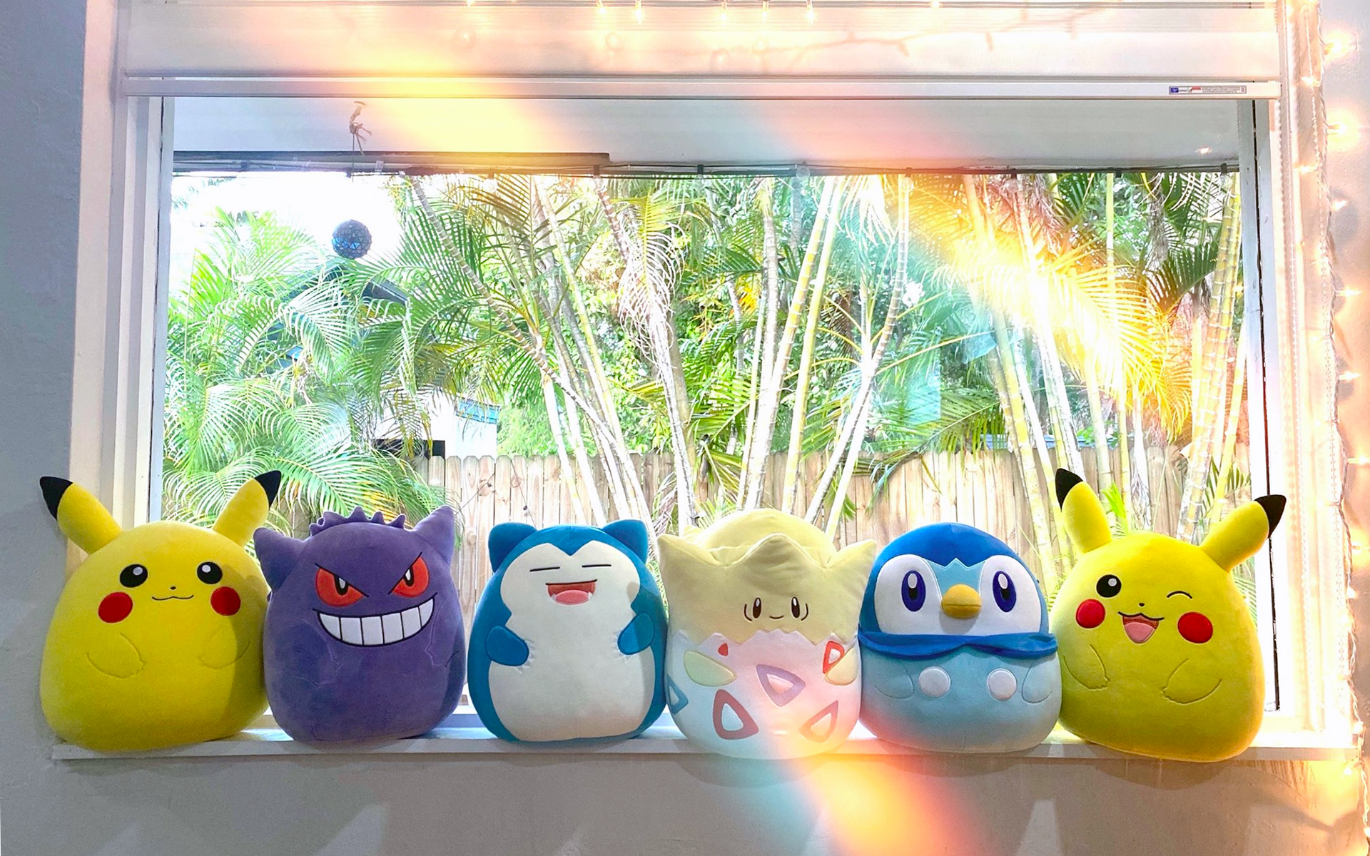 A lineup of Pokémon Squishmallows for Pikachu, Gengar, Snorlax, Togepi, Piplup and winking Pikachu sitting on a window sill