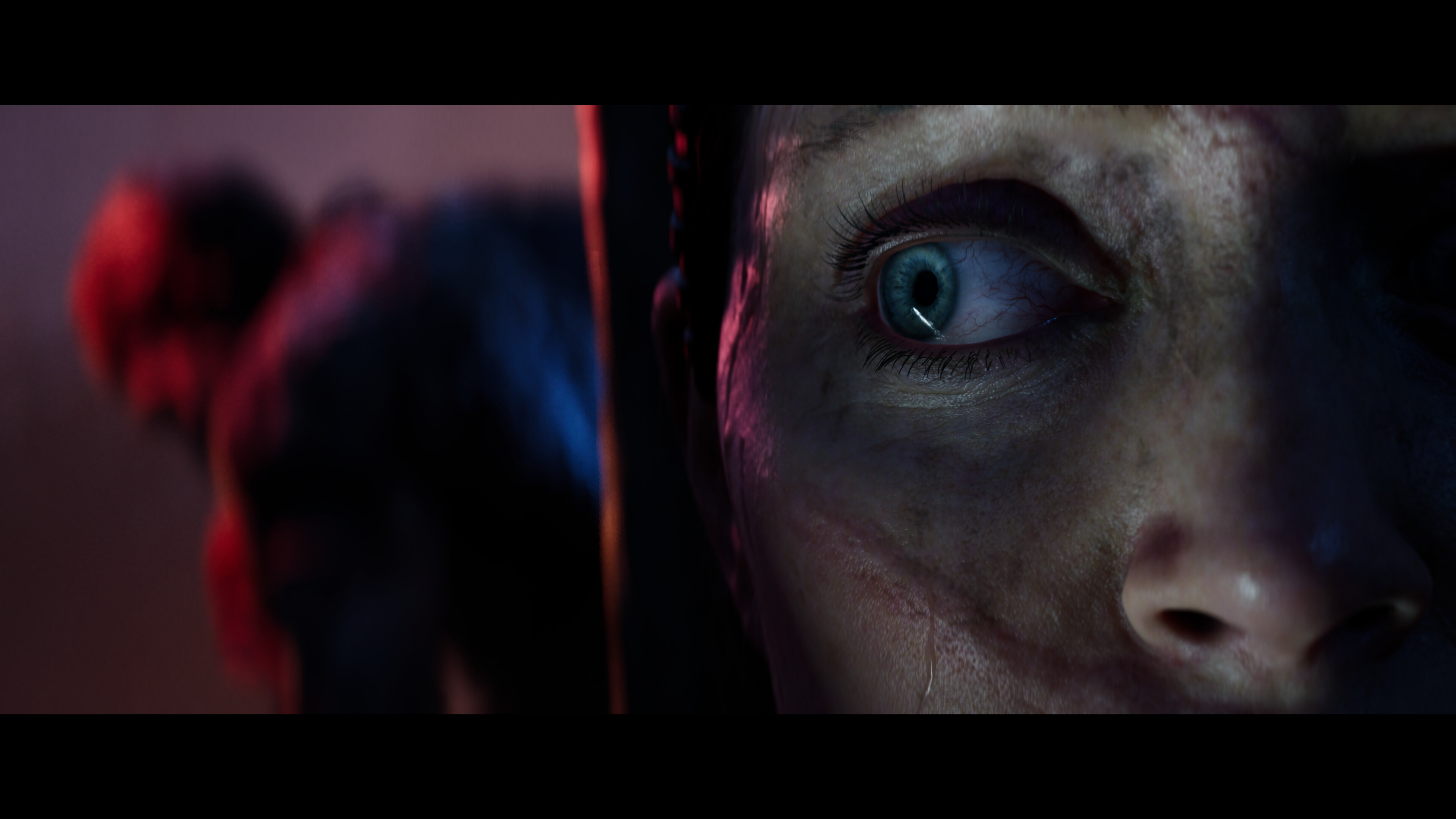 An extreme close-up of Hellblade 2’s Senua glancing to her right - in the background is another figure, out of focus