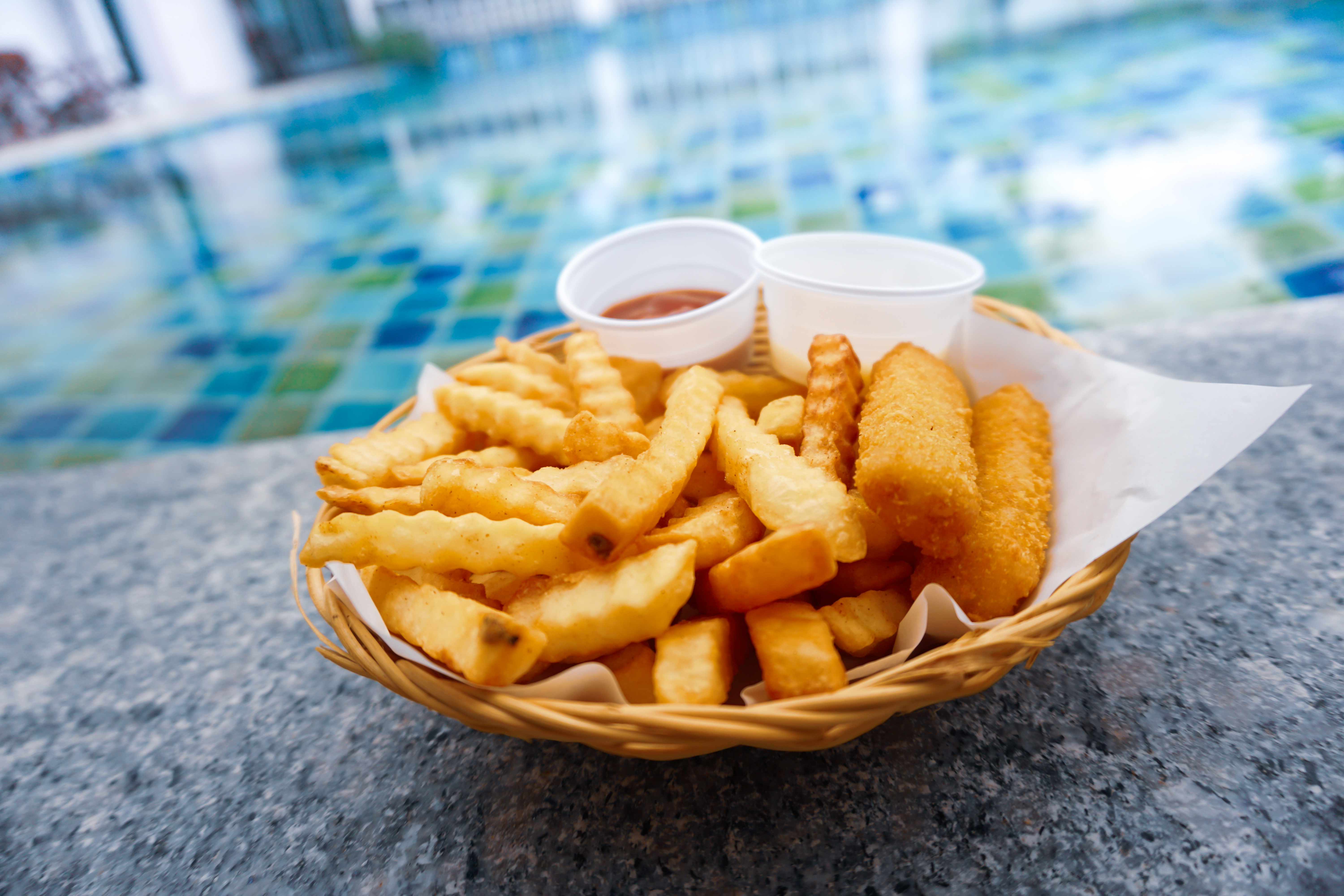 Basket of french fries sit alongside a pool.