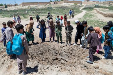 Children gather around a crater after Afghan deminers from the Halo Trust detonated an anti-tank mine in Ghazni province