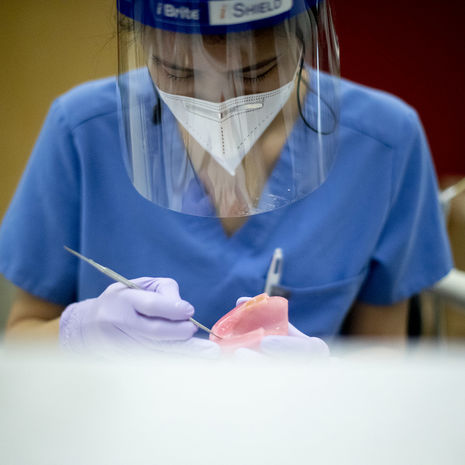 A dental student wearing a mask and face shield 