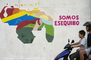 FILE - A boy drives a motorcycle in front of a mural of the Venezuelan map with the Essequibo territory included in the 23 de Enero neighborhood of Caracas, Venezuela, Monday, Dec. 11, 2023. Venezuela President Nicolás Maduro on Wednesday, April 3, 2024, promulgated a law for the creation of the Essequibo state as part of Venezuela, following the referendum held last December to annex to the country the territory rich in minerals and oil that is in dispute with Guyana. (AP Photo/Matias Delacroix, File)