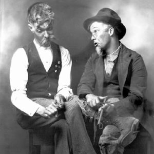 Two white men in costume sitting on a wooden bench