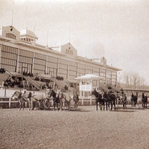 Race horses and men on track next to stands