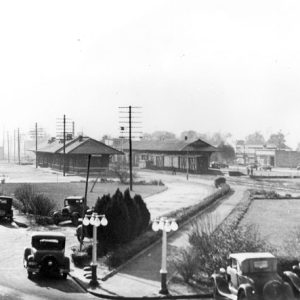 Train depot entrance with parked cars, landscaped sidewalk, town in background
