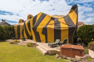 A black and yellow fumigation tent covering a large house. Patio furniture is in front.