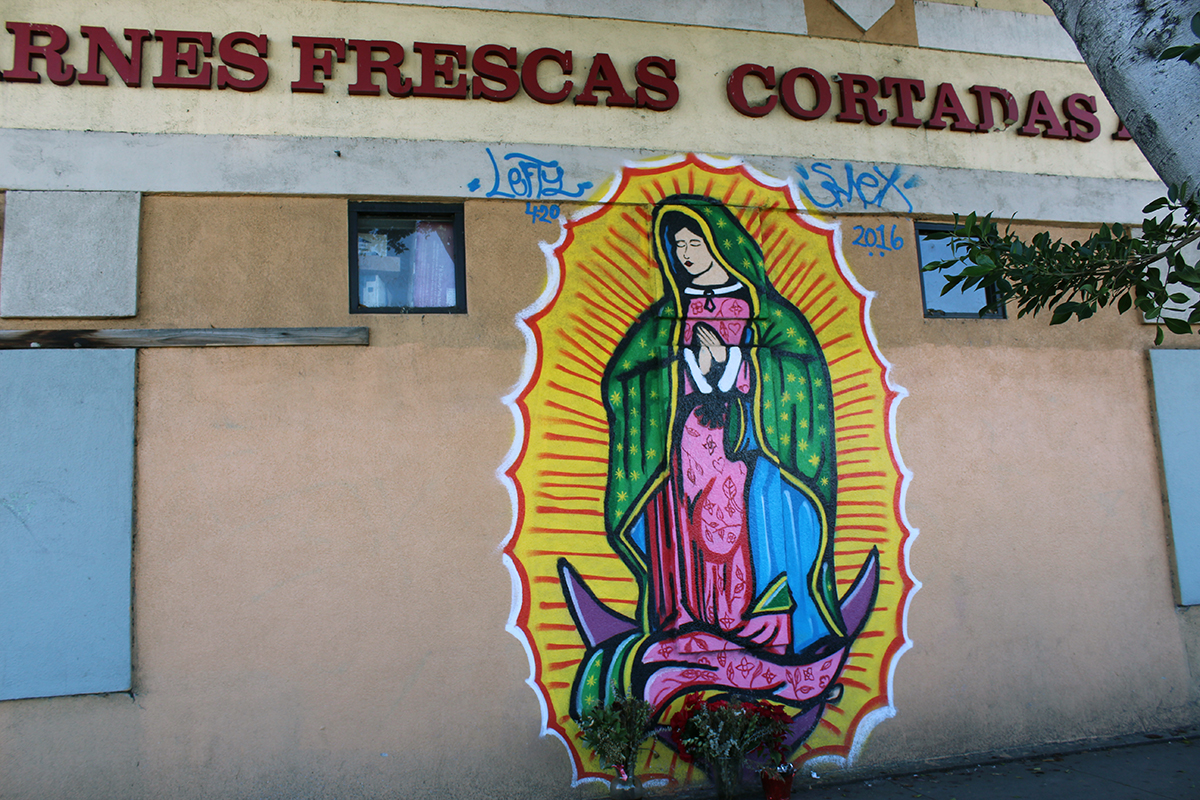 Mural on the side of a building, with the virgin in pink dress and green shawl.