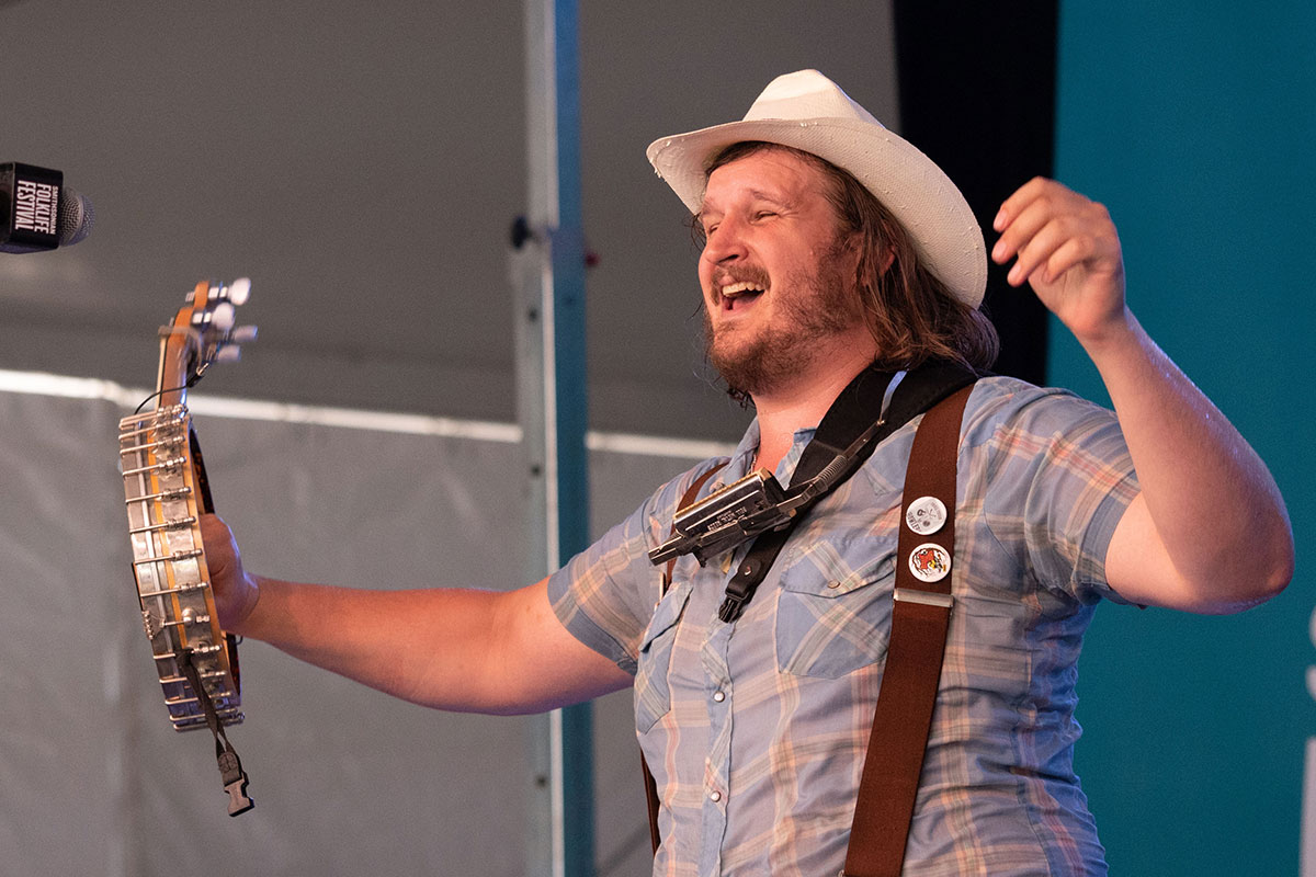 A man holds a banjo and sings on stage.