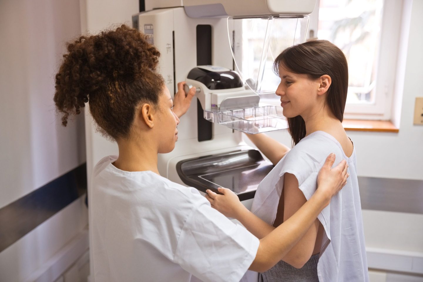 Female doctor talking to young woman during Mammography test in examination room