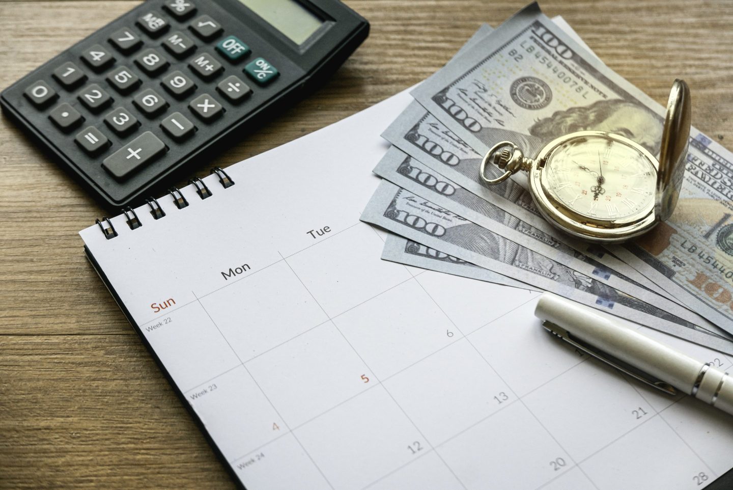 Tax time and saving money and financial planning concept. Calculating monthly expenses. Finance debt collection deadline. Money, calendar, clock and calculator on wooden table.