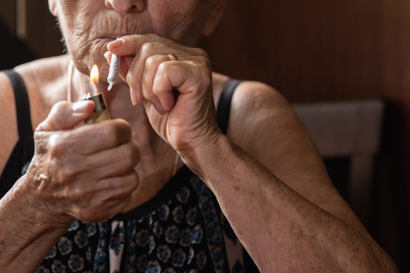 Unrecognizable old woman lighting a joint of marijuana with the flame of a lighter. concept of medical cannabis and CBD and THC.