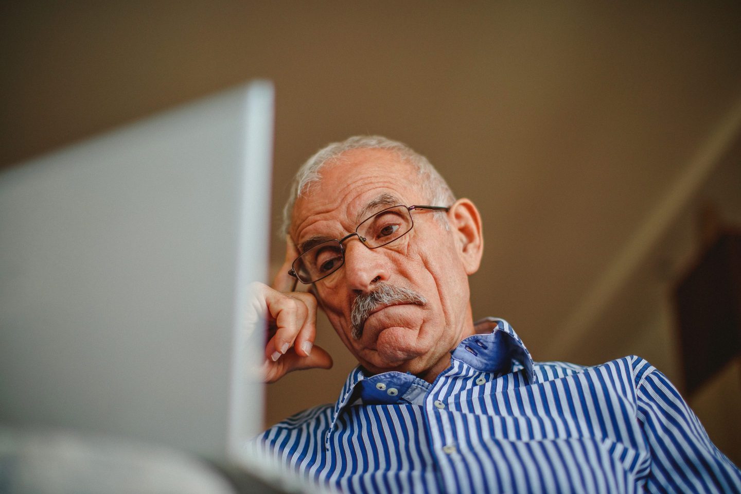 Old depressed senior man at home using laptop