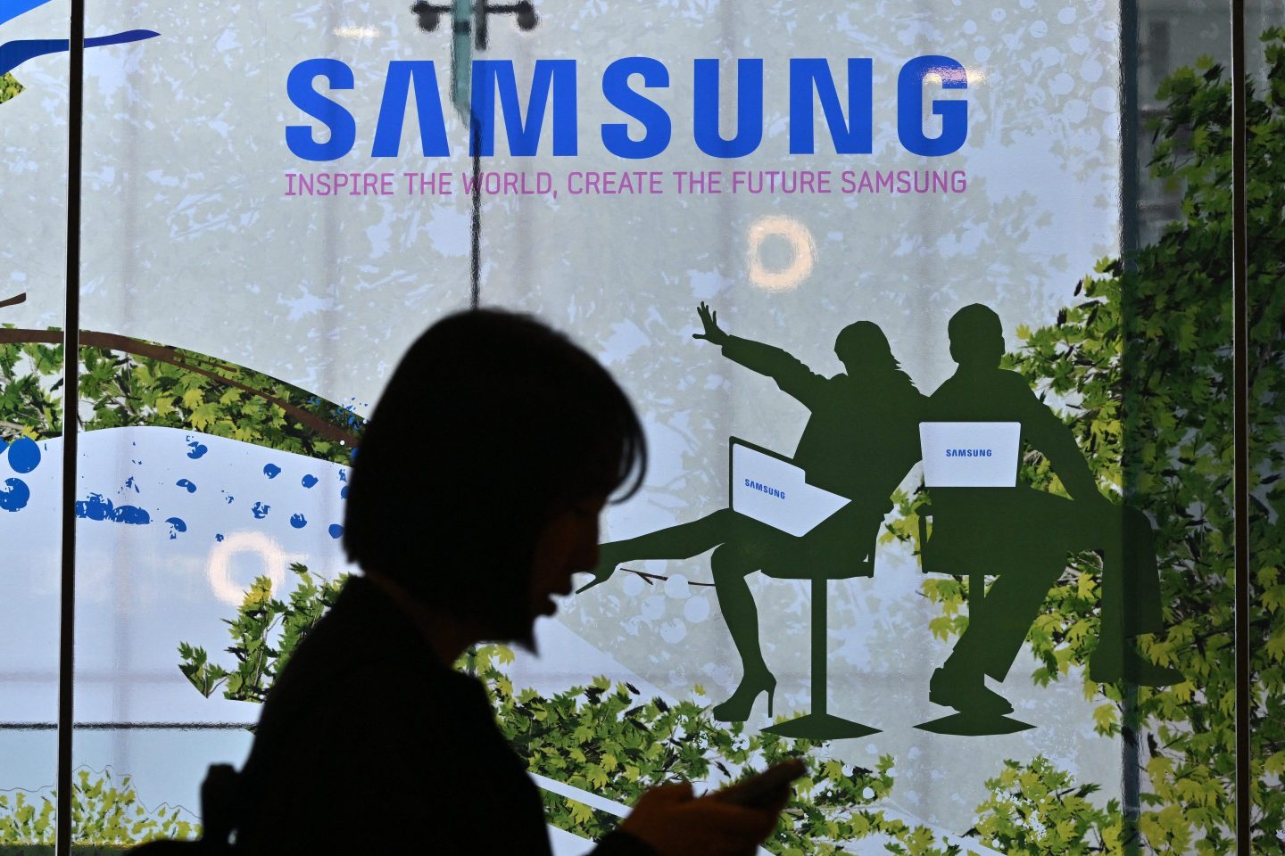 A woman walks past the Samsung logo displayed on a glass window at the company's Seocho building in Seoul on April 30, 2024.