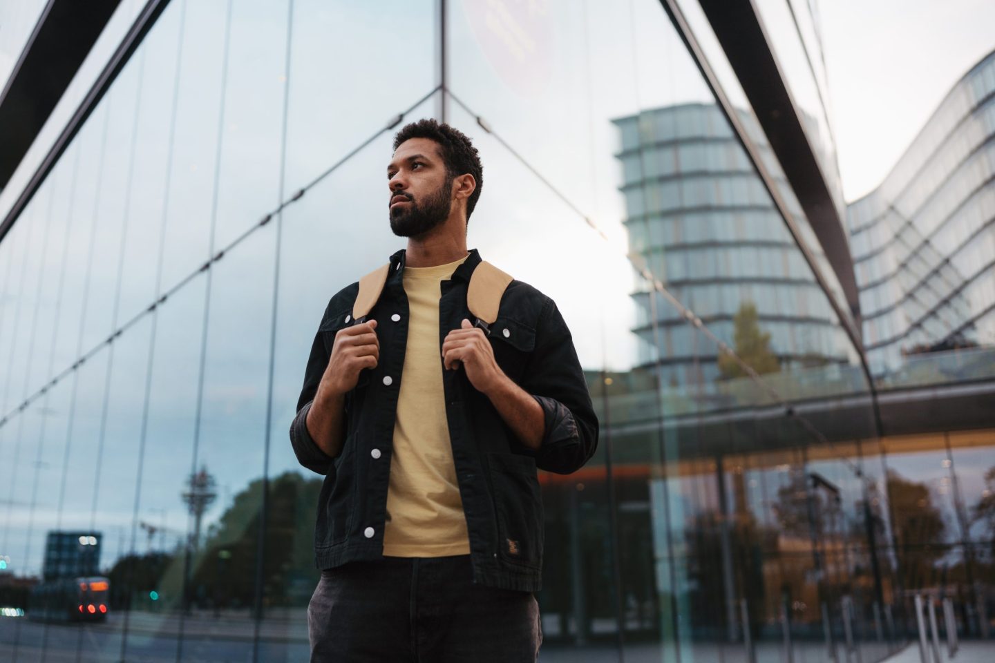 Portrait of young university student in the city standing in front of mirrored glass building. Single man starting his first job. New start, milestone or new beginning for young single man.
