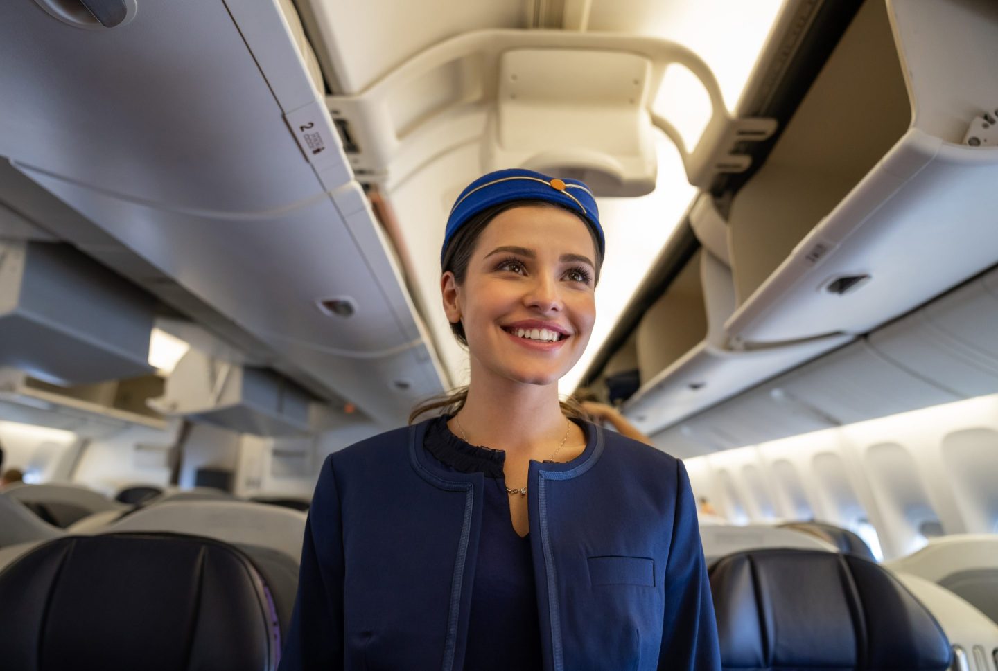 Portrait of a friendly flight attendant smiling on the aisle in an airplane and smiling &#8211; travel concepts