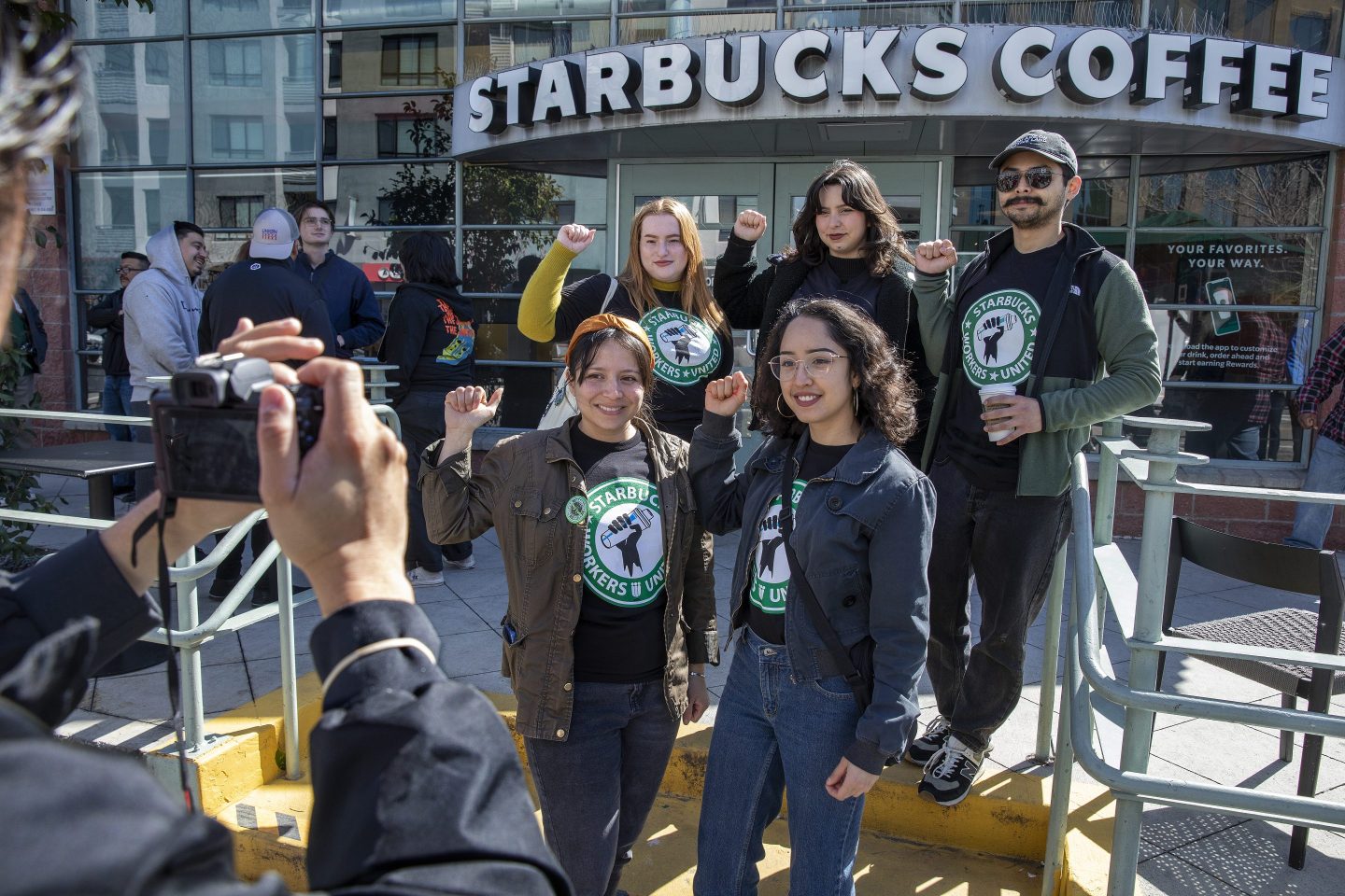 LOS ANGELES, CA-MARCH 24, 2023: Clockwise from top left-Former Starbucks employee Emily Wheeler, and current Starbucks employees Veronica Gonzalez, Jesse De La Cruz,  Kat Ramos and Leila Trejo, stand together for a photograph in front of a Starbucks Coffee located on Central Ave. in downtown Los Angeles, at conclusion of a press conference they attended to announce SB 627-the Displaced Workers Transfer Rights Act, that will hold corporate chain employers accountable for using store closures in a discriminatory or retaliatory manner and give the workers preferential transfer options to other store locations.  (Mel Melcon / Los Angeles Times via Getty Images)