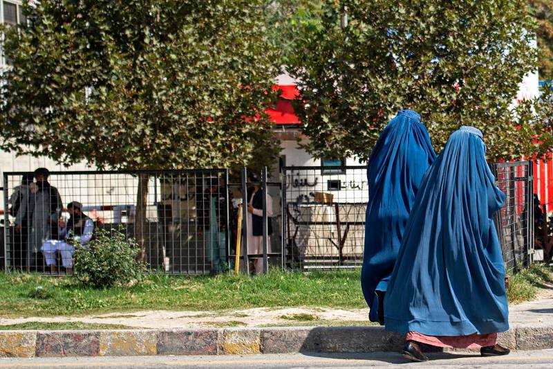 Two Afghan women in blue burqas walk past the gated embassy building.