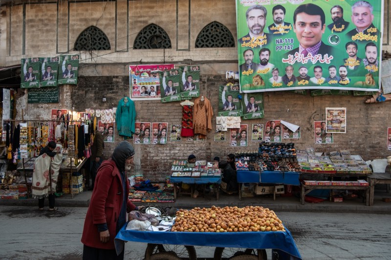 People walk past market stalls under banners depicting candidates from different political parties ahead of the elections in Lahore, Pakistan, on Feb. 7.