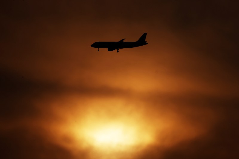 A commercial airline aircraft flies past clouds as the sun sets over Kuwait City.